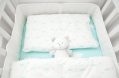 small,,white,teddy,bear,in,baby,bed.,linen,with,clouds.